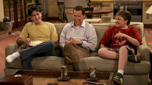 Two and a half men. 3 Männer sitzen lachend auf der Couch