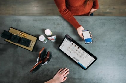 mann sitzt vor Tablet einer Frau gegenüber, die ein Handy in der Hand hält