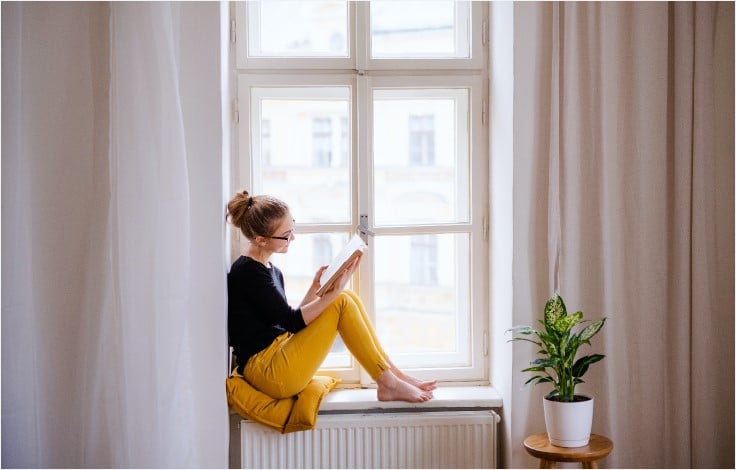Frau liest Roman auf Fensterbank