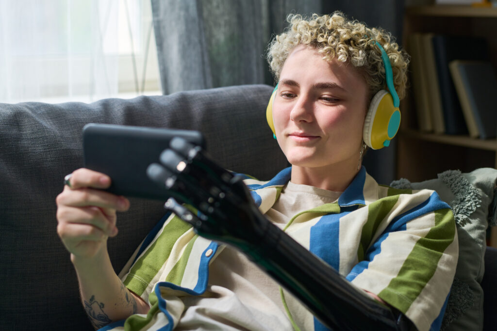 Happy girl with myoelectric arm watching online movie in smartphone on sofa