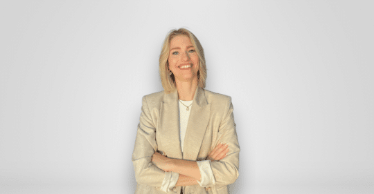Desiree Novak steht lächelnd vor einem hellen Hintergrund